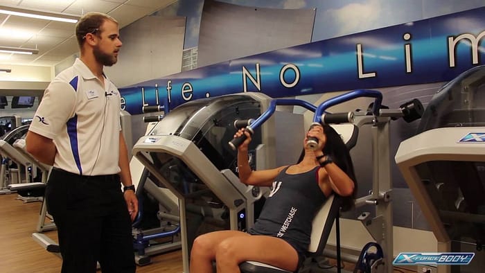 Woman using a tilting weight stack with her personal trainer nearby
